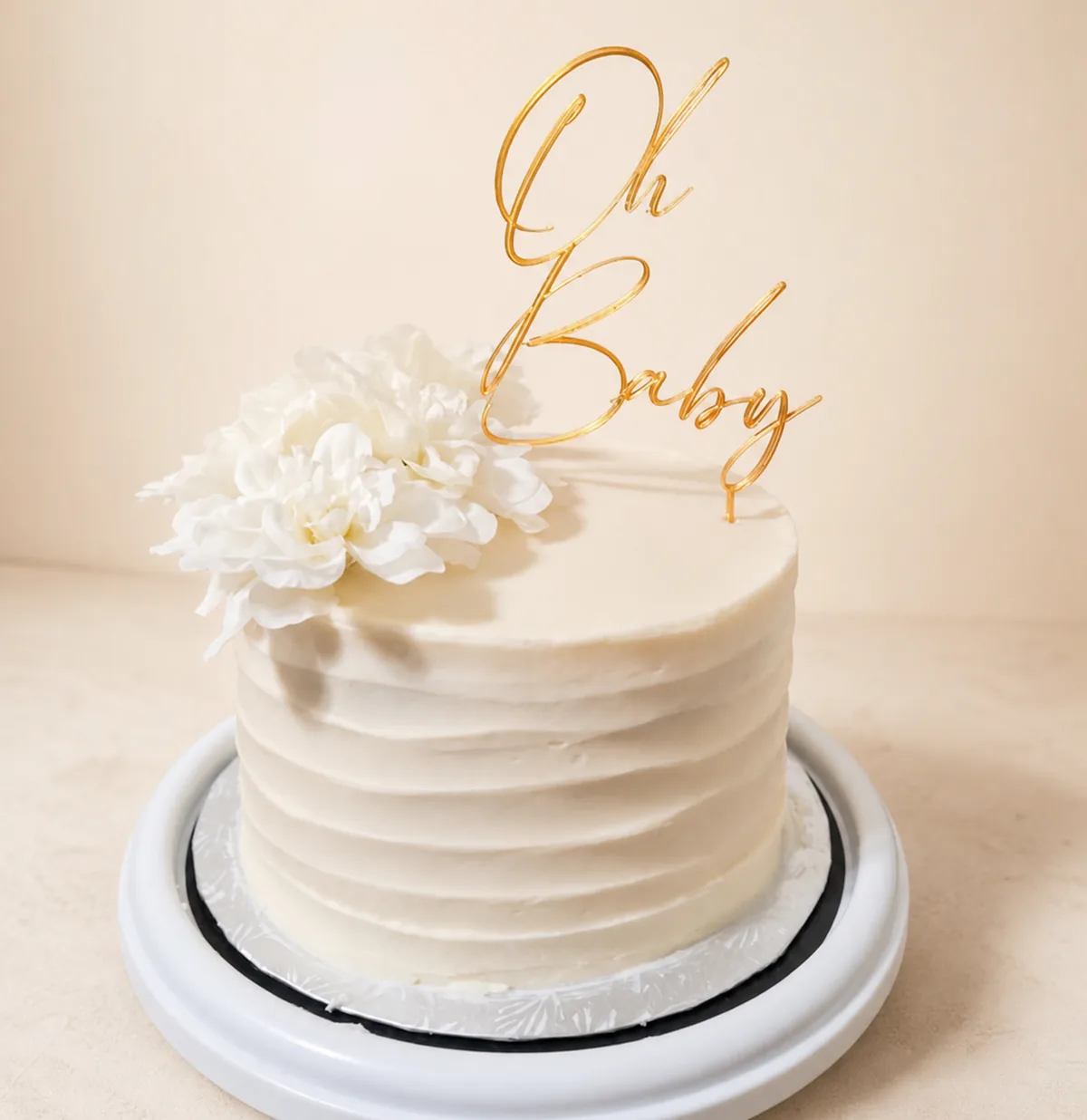Gold Oh Baby topper on a cream cake with white flowers